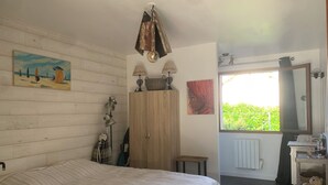 A bedroom with a bed, a wooden wardrobe, a window with a view, and a painting on the wall. - Maison Clôturée, Plages, Lacs, Océan et Jacuzzi. Animaux de Compagnie Acceptés (Escource)