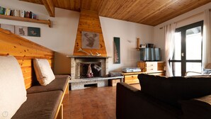 A cozy living room with a stone fireplace, wooden beams, a television, and a bookshelf. - Italianway - Capitano Grandi 5 (Bormio)