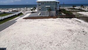 Una casa frente a la playa de dos pisos con balcón, una playa arenosa al frente y el océano al fondo.