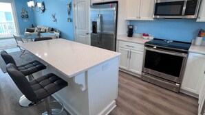Una cocina moderna con armarios blancos, electrodomésticos de acero inoxidable y una isla central con taburetes de bar.