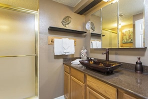 Un baño con un espejo grande, un lavamanos pedestal, armarios de madera y decoración mural.