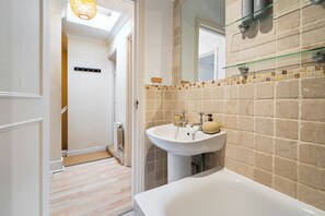 Une salle de bain moderne avec un lavabo blanc, des carreaux de couleur beige et une étagère en verre au-dessus du miroir.