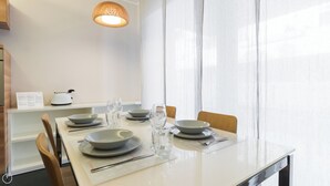 Un comedor con una mesa dispuesta para cuatro personas, incluyendo platos, tazones, vasos y cubiertos. Se ve una tetera y un menú en la encimera.