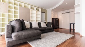 A modern living room with a sectional sofa, a large white rug, wooden flooring, built-in shelving, and a dark wooden cabinet. - Italianway - Cavour 75 (Cernusco sul Naviglio)