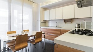 Cocina moderna con estufa a gas, un lavamanos y armarios de madera. Hay una zona de comedor con una mesa y sillas.