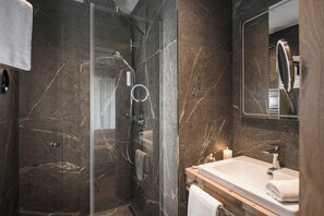 Features a glass-enclosed shower, wooden vanity, and large mirror.