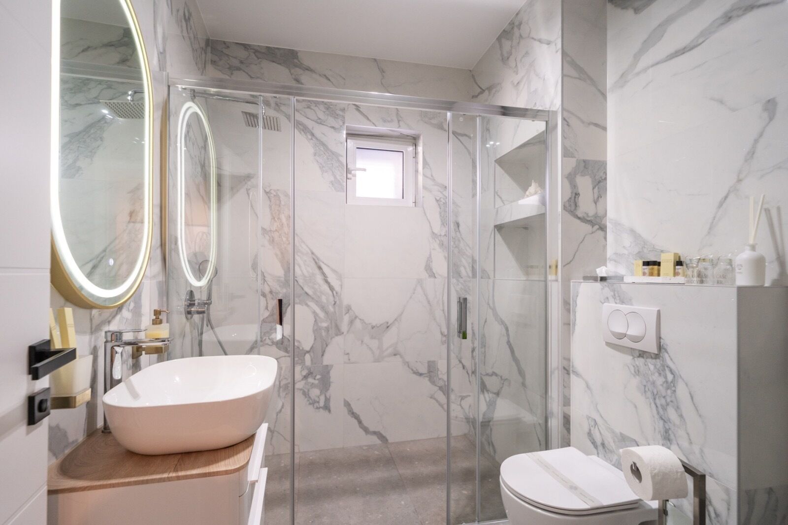 Un baño moderno con un lavamanos grande de mármol, una ducha con mampara de vidrio y un inodoro.