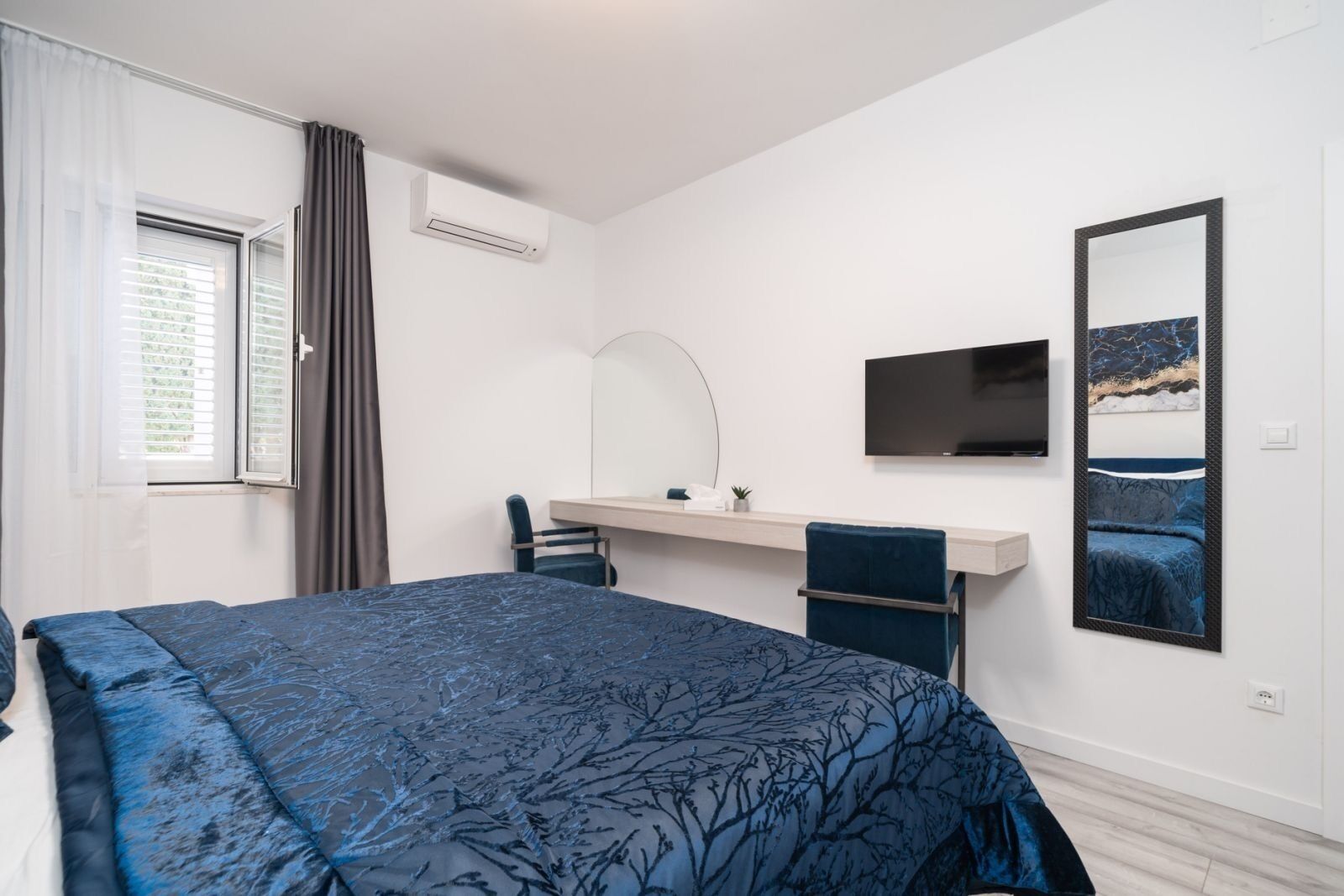 A bedroom with a large bed, a desk, a chair, a TV, and a painting on the wall.
