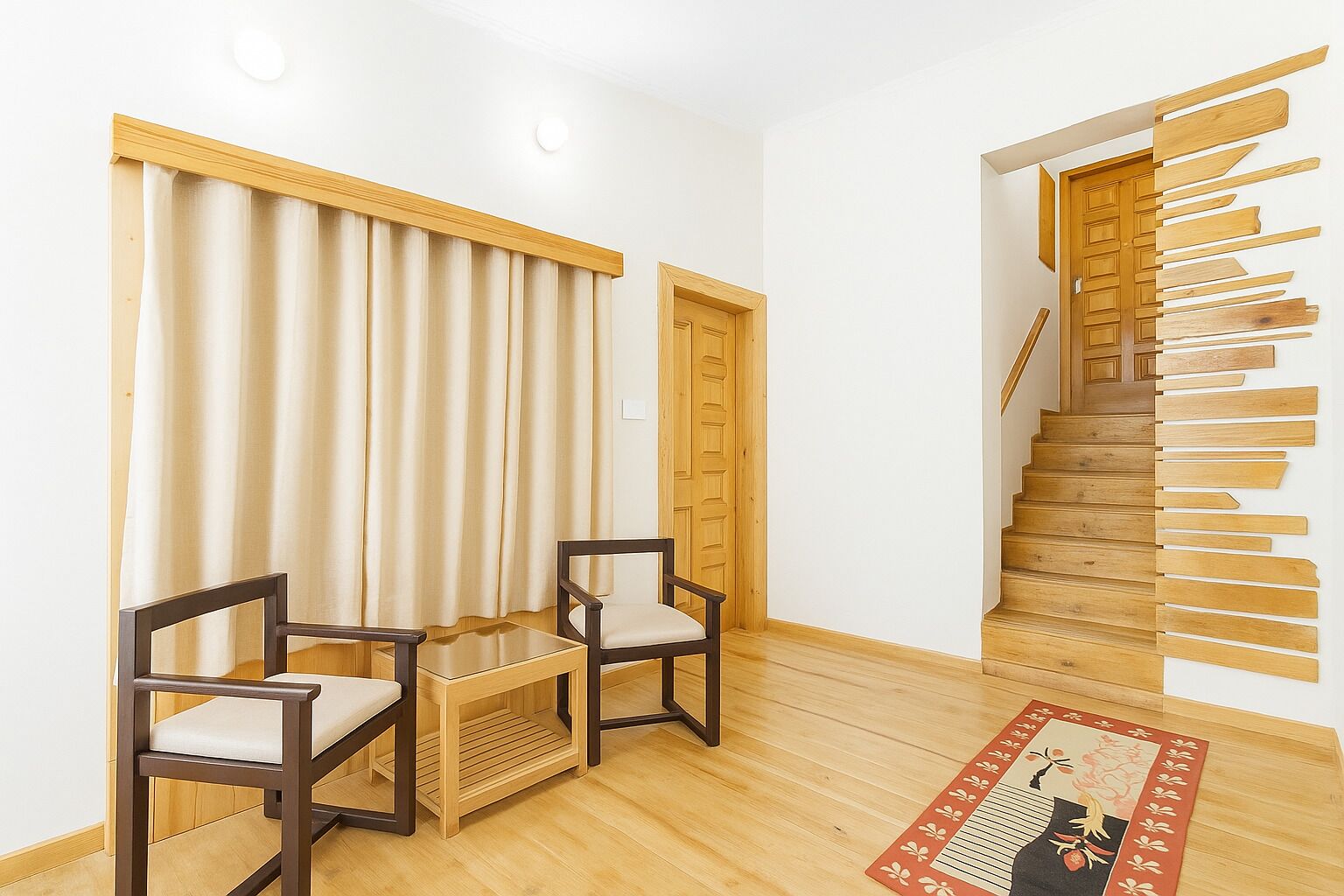 Een kamer met een houten trap, twee stoelen, een tafeltje en een rood kamerkleed met een patroon.