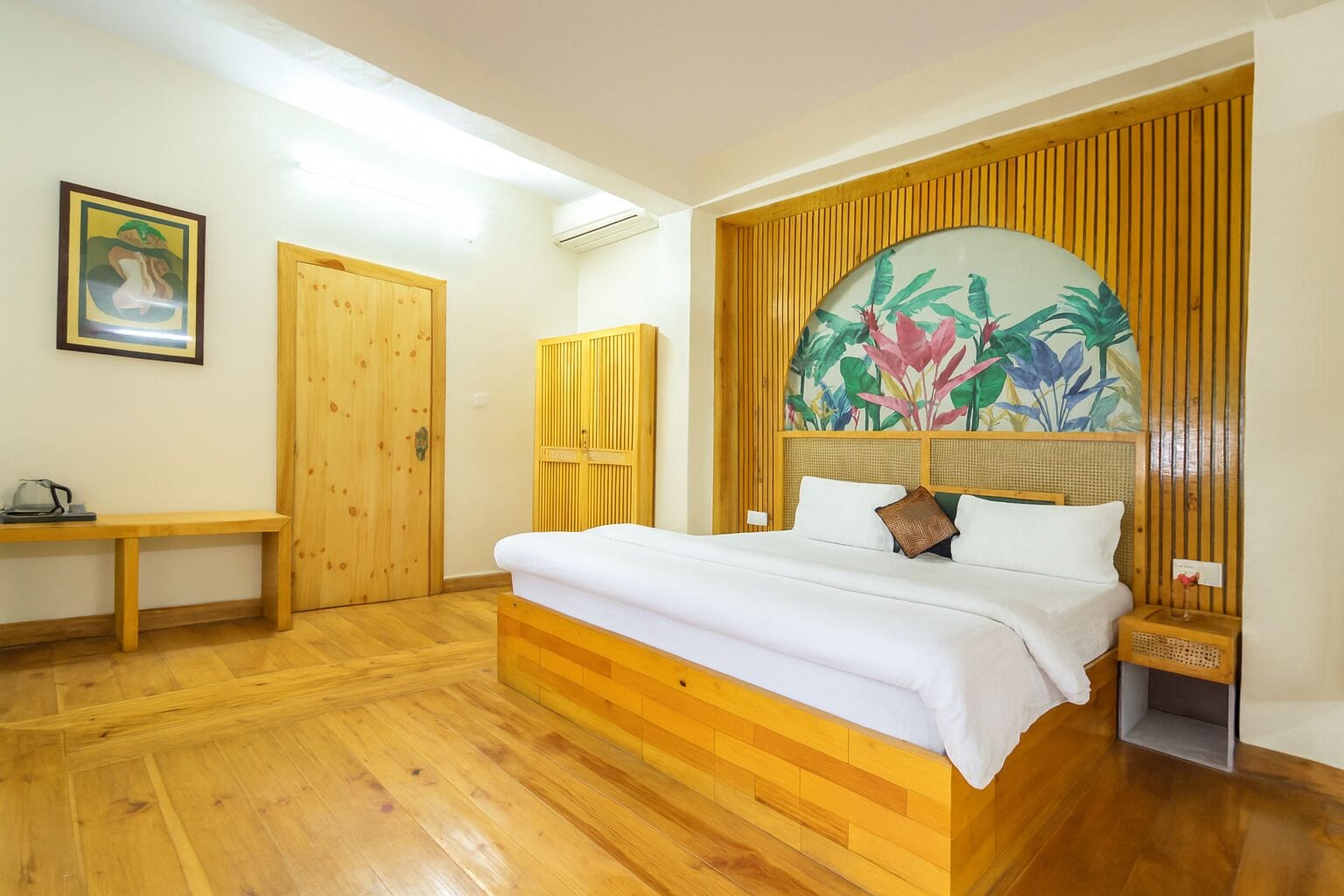 Quarto com cama de madeira, um banco, uma porta e uma parede com mural de plantas tropicais.