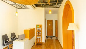 Zona de recepción con un escritorio de madera, una computadora, una estantería con objetos y una lámpara.