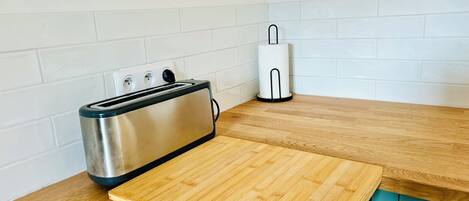 Una cocina con un tostador, un dispensador de toallas de papel y una tabla de cortar de madera sobre la encimera.