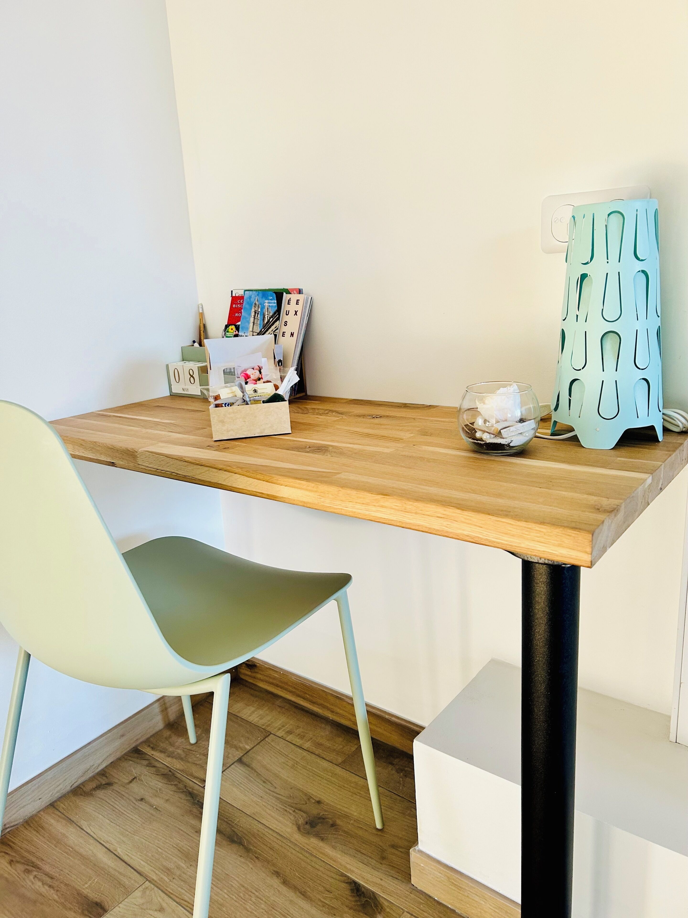 Een houten tafel met een witte stoel, een klein glazen potje en een decoratief object op tafel.