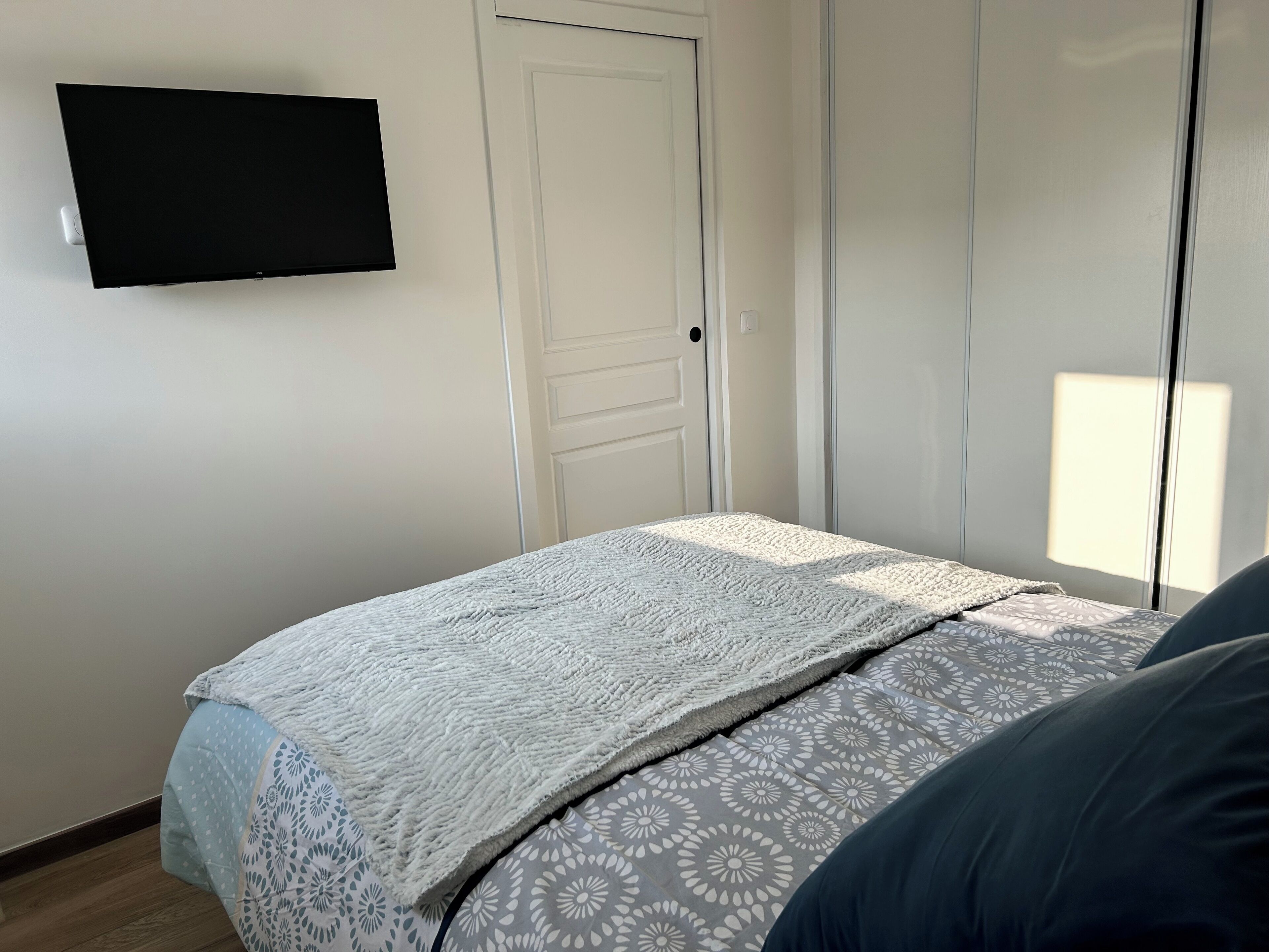 Une chambre à coucher avec un lit, un téléviseur fixé au mur et une porte.