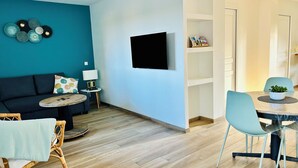 Una sala moderna con un sofá azul oscuro, una mesa redonda de centro, una mesita auxiliar con una lámpara, y un comedor con una mesa y sillas redondas.