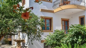 A white building with balconies, a stone fountain, and lush greenery. - Eva Studios & Apartments (Malevizi)