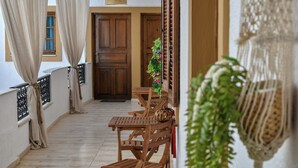 A wooden balcony with a table and chairs, a hanging light fixture, and a door in the background. - Eva Studios & Apartments (Malevizi)
