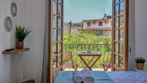 A balcony with a table and chairs, a bed with rolled towels, a potted plant, and decorative plates on the wall. - Eva Studios & Apartments (Malevizi)