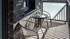 Un balcon avec deux fauteuils en osier et une petite table ronde, une porte vitrée et un mur en briques.