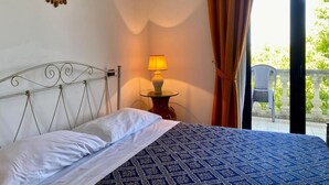 A bed with a patterned bedspread, a bedside lamp, and a view of greenery outside.