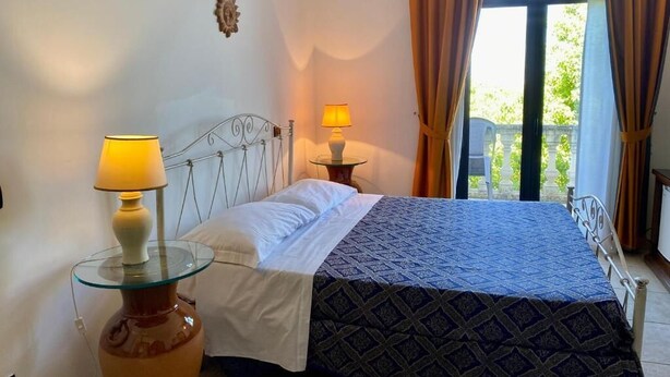 A bedroom with a bed, two bedside lamps, a vase, and a window with curtains.
