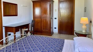 A hotel room with a bed, a desk, a wardrobe, and a bedside table with a lamp.