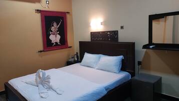 A hotel room with a bed, a nightstand, a wall-mounted air conditioner, a decorative tapestry, a wall-mounted light, and a mirror.
