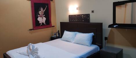 Hotelkamer met een bed, nachtkastje, een wandairconditioner, wandtapijt, wandlamp en spiegel.