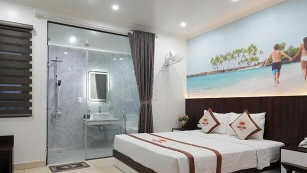 A hotel room with a large bed, a glass shower enclosure, a bathroom with a sink, and a mural of a beach scene.