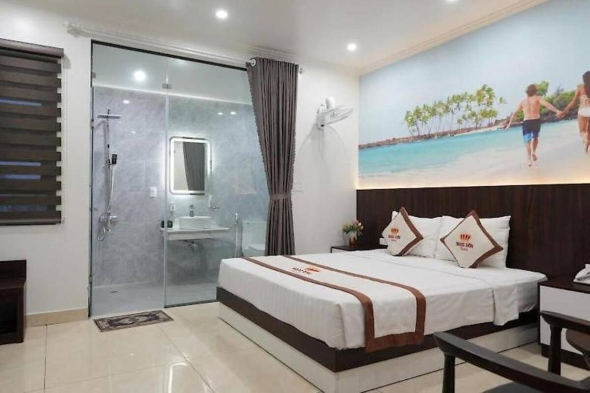 Ein Hotelzimmer mit einem großen Bett, einer Dusche mit Glastrennwand, einem Badezimmer mit Waschbecken und einem Wandbild mit einer Strandansicht.
