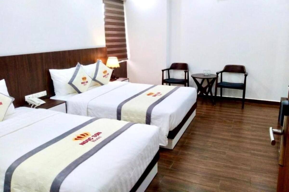 Ein Hotelzimmer mit zwei Betten, einem kleinen Tisch mit Stühlen, einer Lampe und einer Klimaanlage an der Wand.