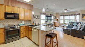 Eine geräumige Küche mit Holzausstattung, einer eingebauten Mikrowelle und einem Backofen. Es gibt eine Essecke mit Tisch und Stühlen, sowie ein Wohnzimmer mit einer Couch und einem Deckenventilator.