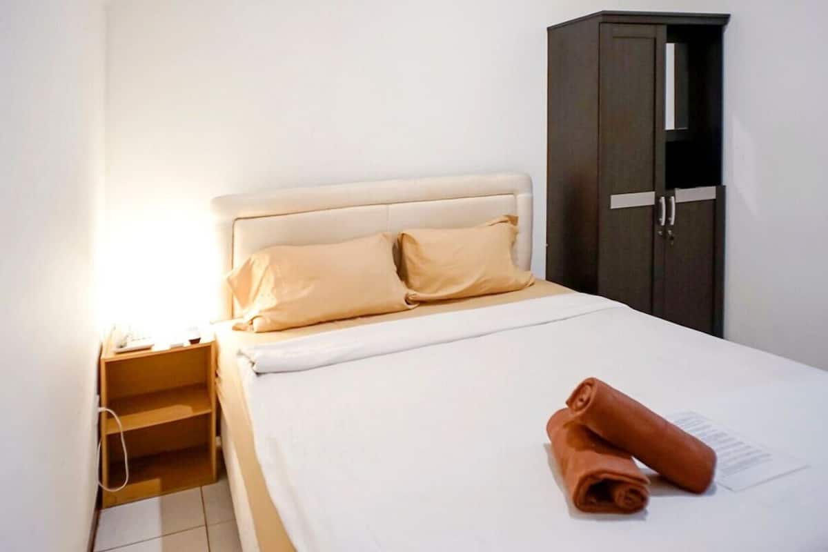 A hotel room with a bed, a wardrobe, and a nightstand with a lamp.