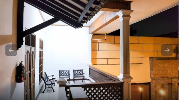 A staircase with a wooden railing, a fire extinguisher, and two chairs. - Kasmaran Guest House Syariah By SIHA Hospitality (Jakarta)