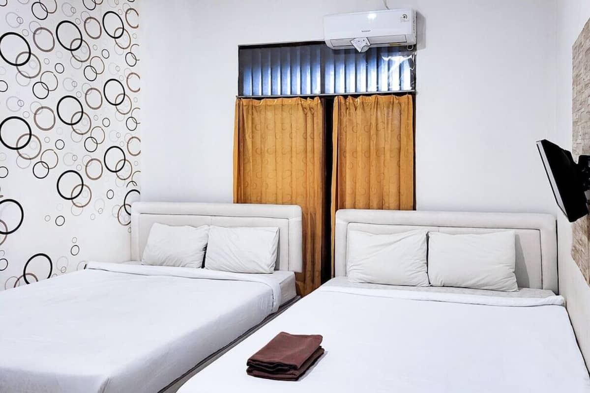 A hotel room with two beds, a TV mounted on the wall, and a window with curtains.