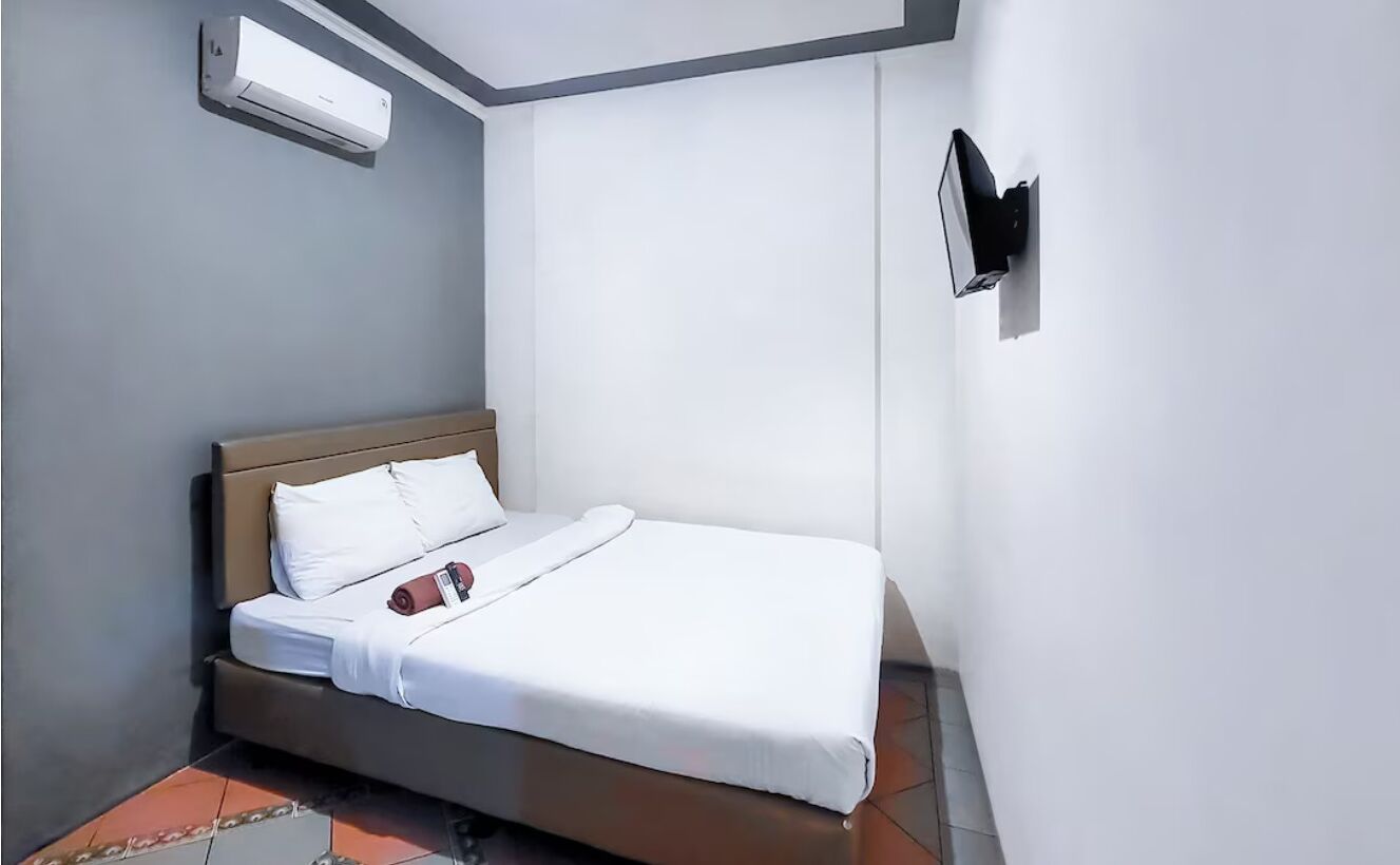 A neatly made bed with white bedding, a wooden headboard, and a red object on the bed.