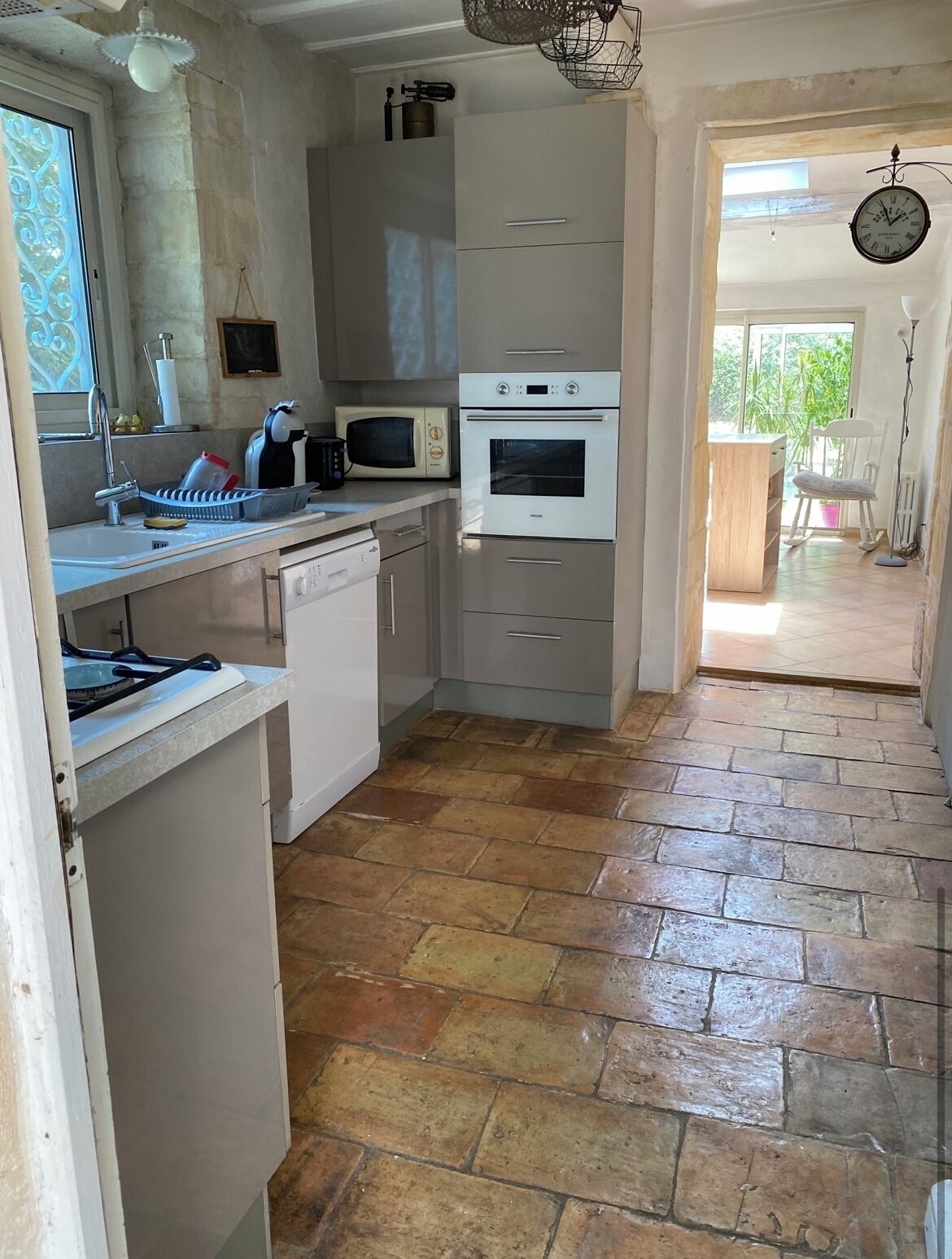 A compact kitchen with a microwave, oven, and a sink. There is a window with decorative glass, and a door leading to an outdoor area.
