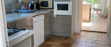 A compact kitchen with a microwave, oven, and a sink. There is a window with decorative glass, and a door leading to an outdoor area.