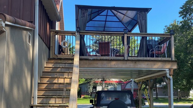 A two-story house with a wooden staircase leading to a balcony. A black SUV is parked in the driveway.