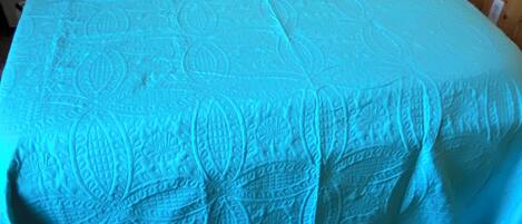 Una cama con una colcha estampada y dos almohadas, un cabecero de metal y una mesita de noche de madera con una lámpara y libros.