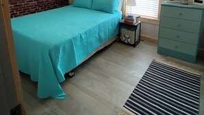 A bedroom with a bed, a dresser, a window, and a brick wall.