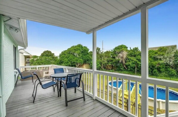 Une terrasse couverte avec une piscine, du mobilier d’extérieur et une vue sur une autre piscine et des arbres.