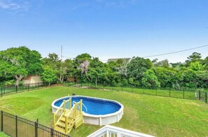 Un jardin avec une piscine, une terrasse en bois et un espace clôturé.