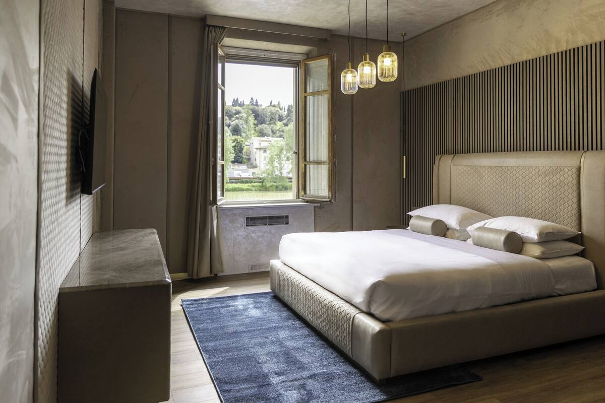 A bedroom with a large bed, a window with curtains, a bedside table, and a hanging light fixture.