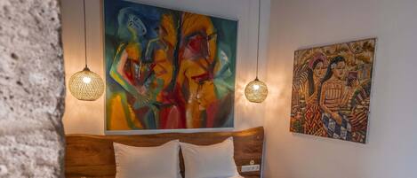 A bedroom with a wooden headboard, a large bed with white bedding, two wall-mounted lamps, and two paintings.