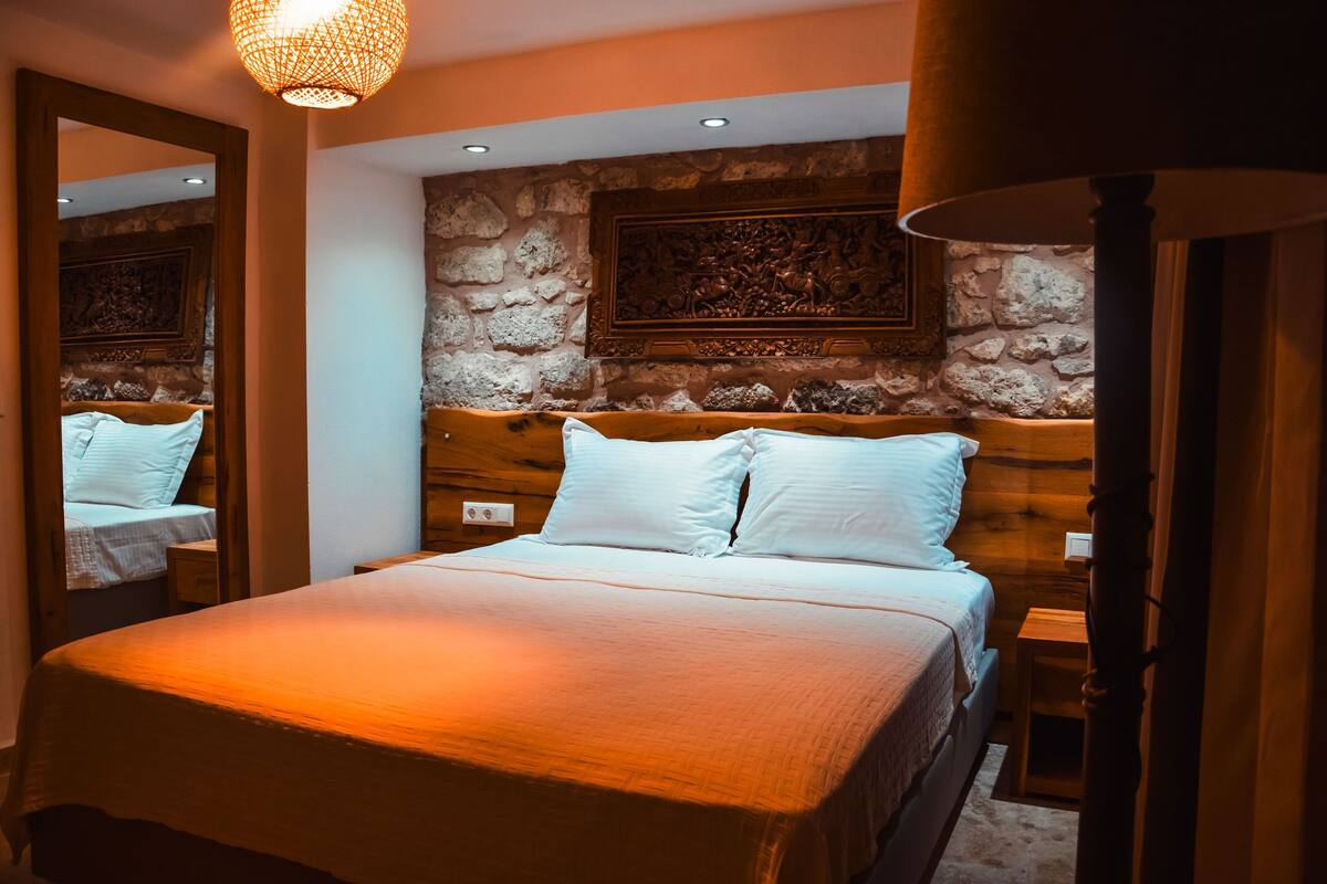 A bedroom with a large bed, wooden headboard, stone wall, and a hanging light fixture.