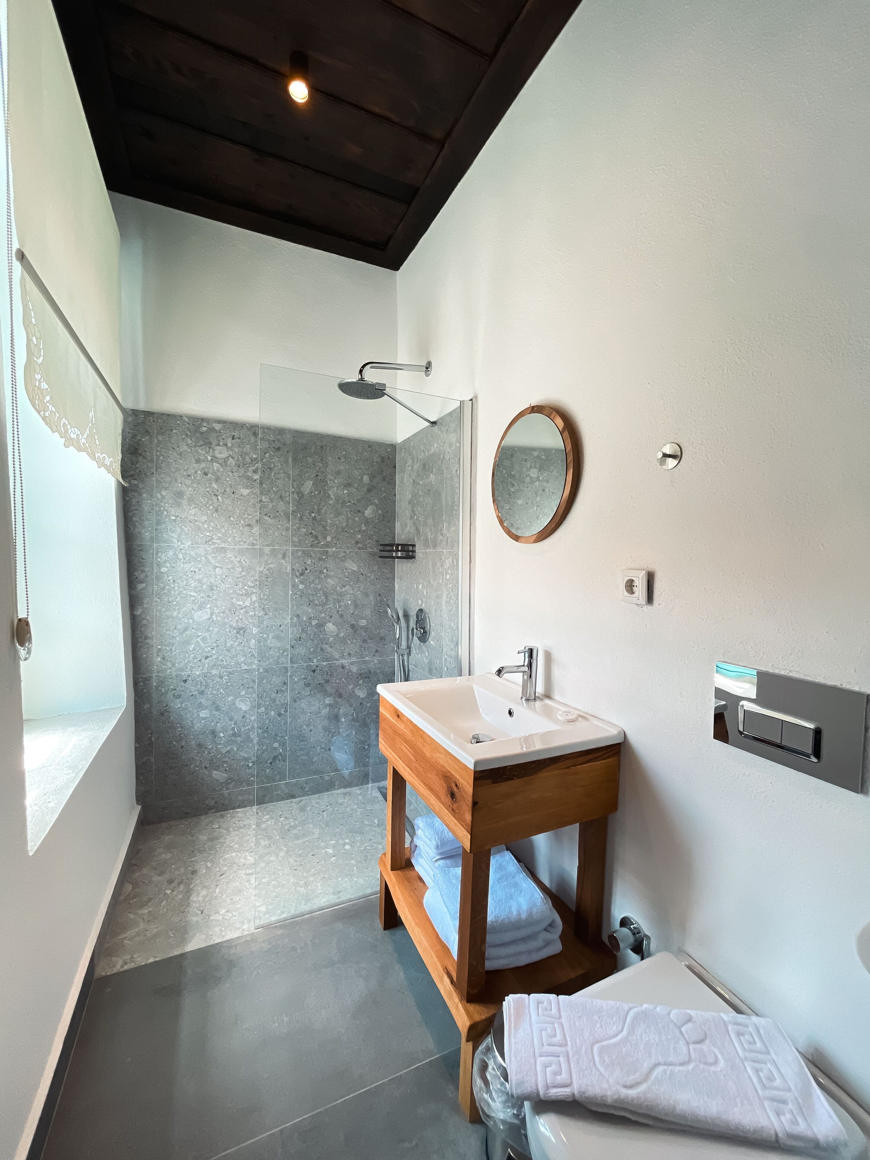 Un baño moderno con ducha, un lavabo con tocador de madera y un espejo en la pared.