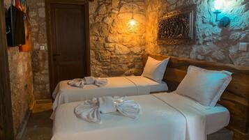 Una habitación con dos camas, paredes de piedra, una puerta de madera y una lámpara fijada a la pared.