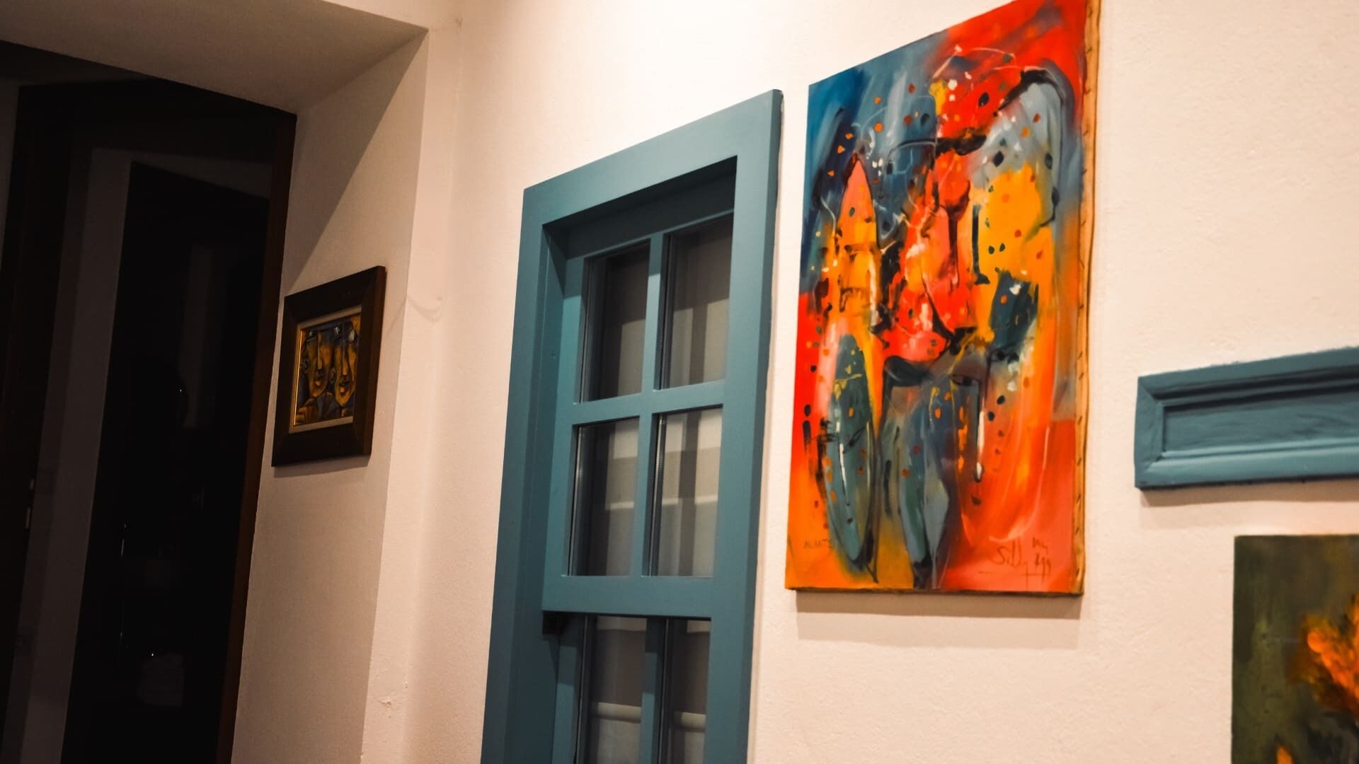 A hallway with a blue-framed window and a colorful abstract painting on the wall.