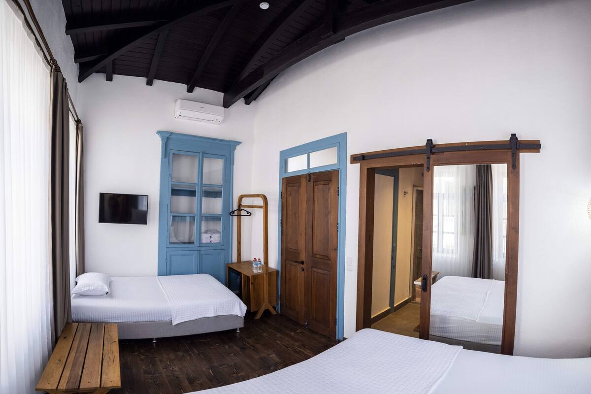 A room with two beds, a wooden table, a TV, and a blue cabinet.